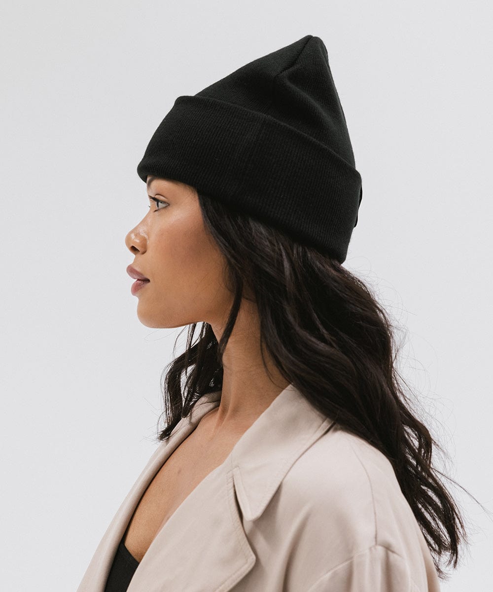 Woman wearing a black beanie and a cream coat, facing sideways against a plain background #color_black