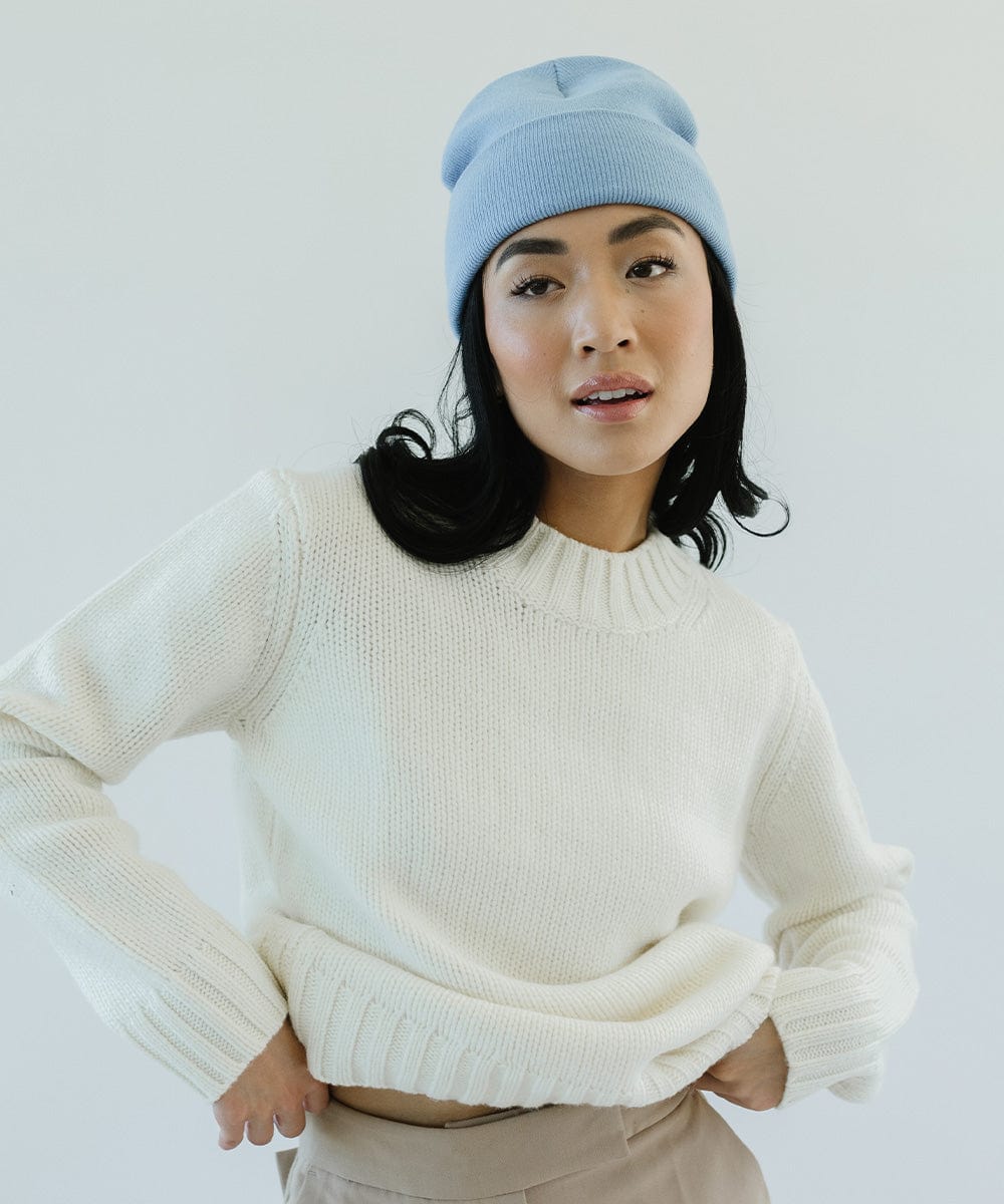Woman wearing an azure blue colored beanie and a white sweater, posing against a plain background #color_azure blue