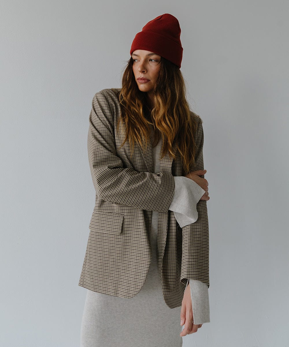 Woman wearing a brick red colored beanie and a grey outfit with a coat, posing against a plain background #color_brick red