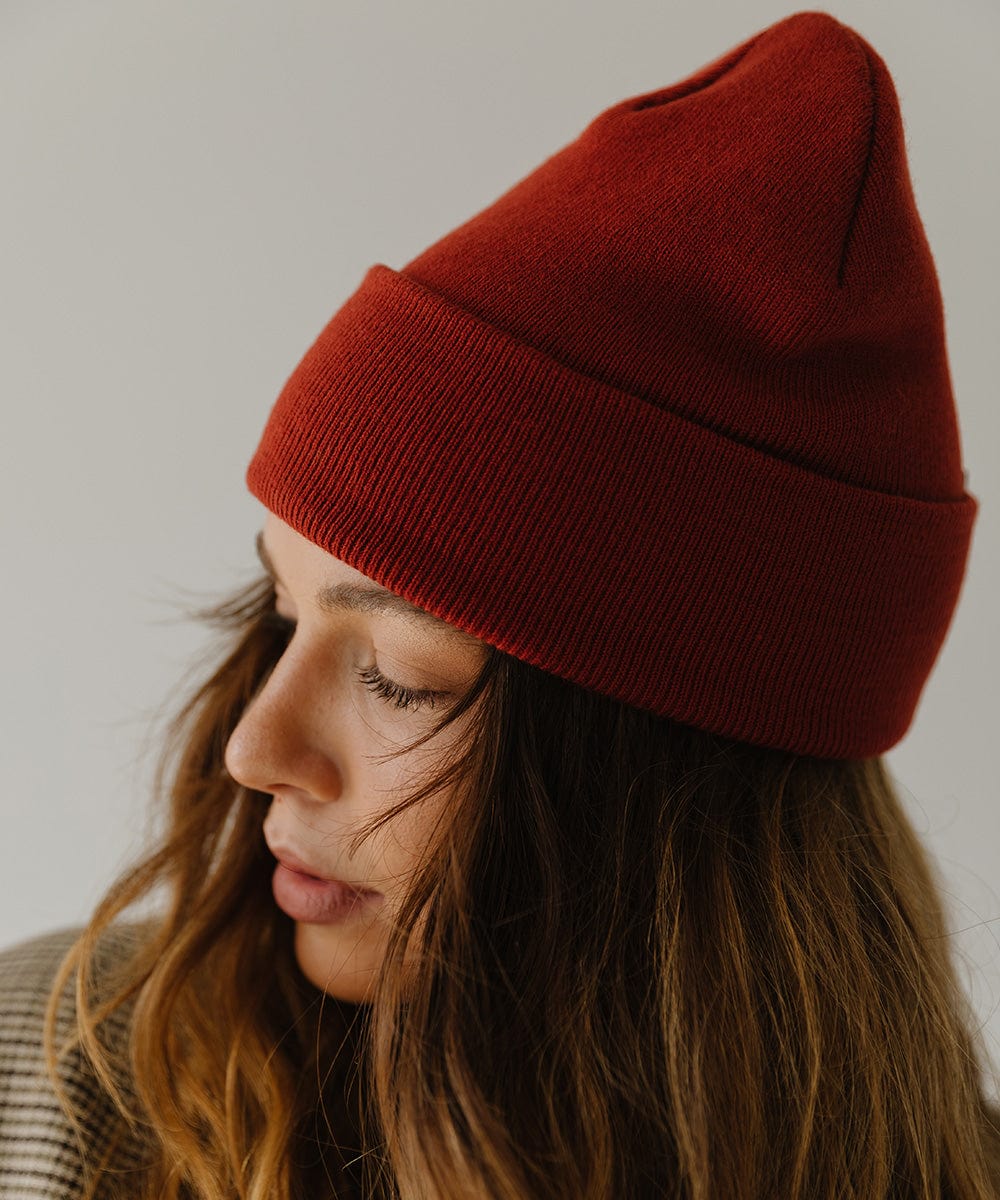 Woman wearing a brick red colored beanie facing sideways against a plain background #color_brick red