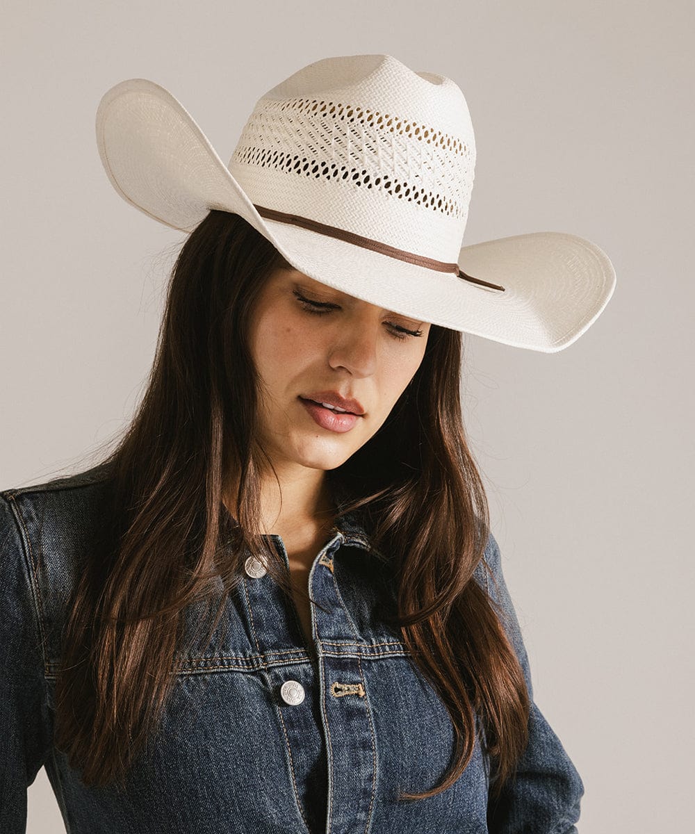 Woman wearing a classic white waxed paper straw cowboy hat with a hat band and a denim shirt against a plain background