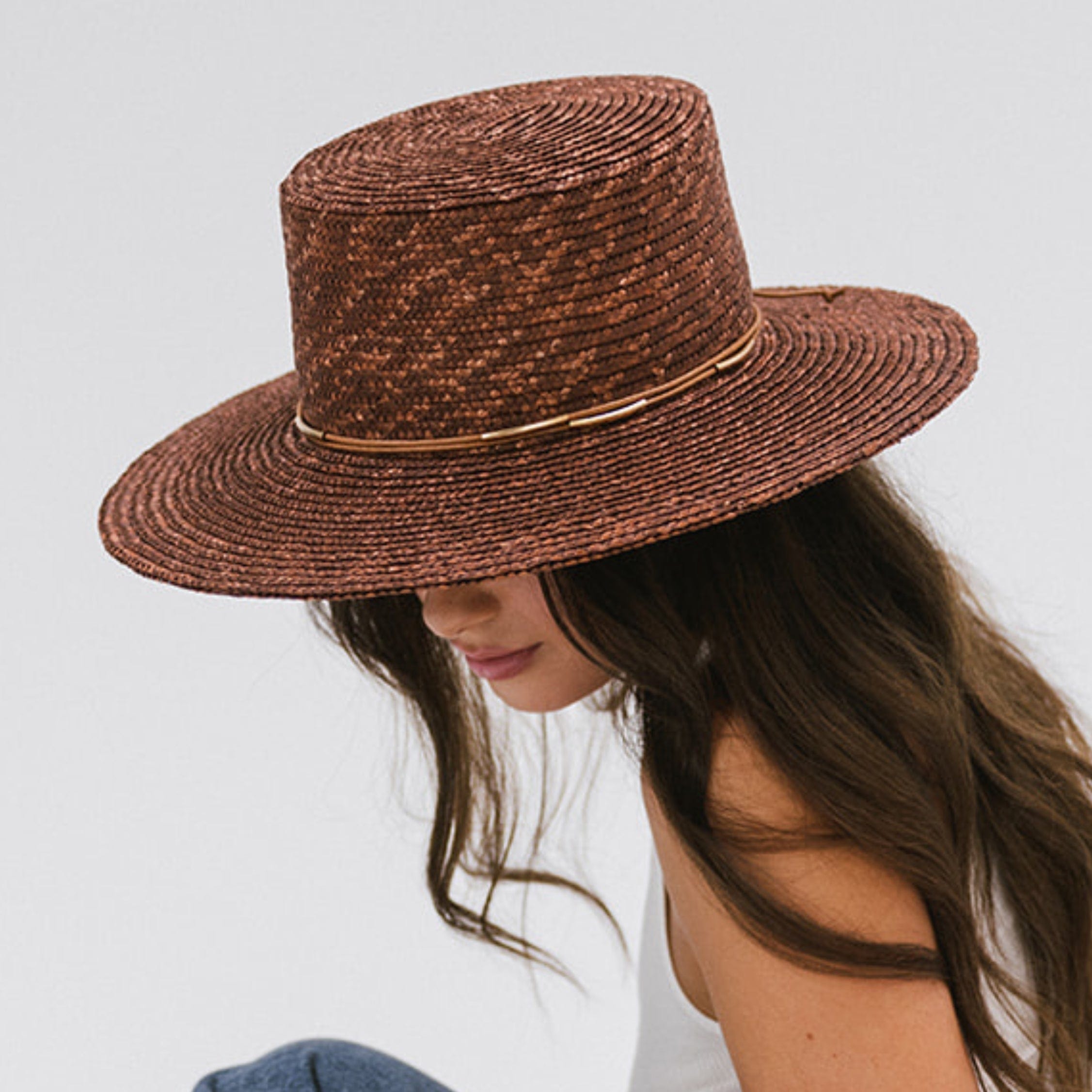 Woman wearing a brown straw hat with a hat band against a plain background #color_brown