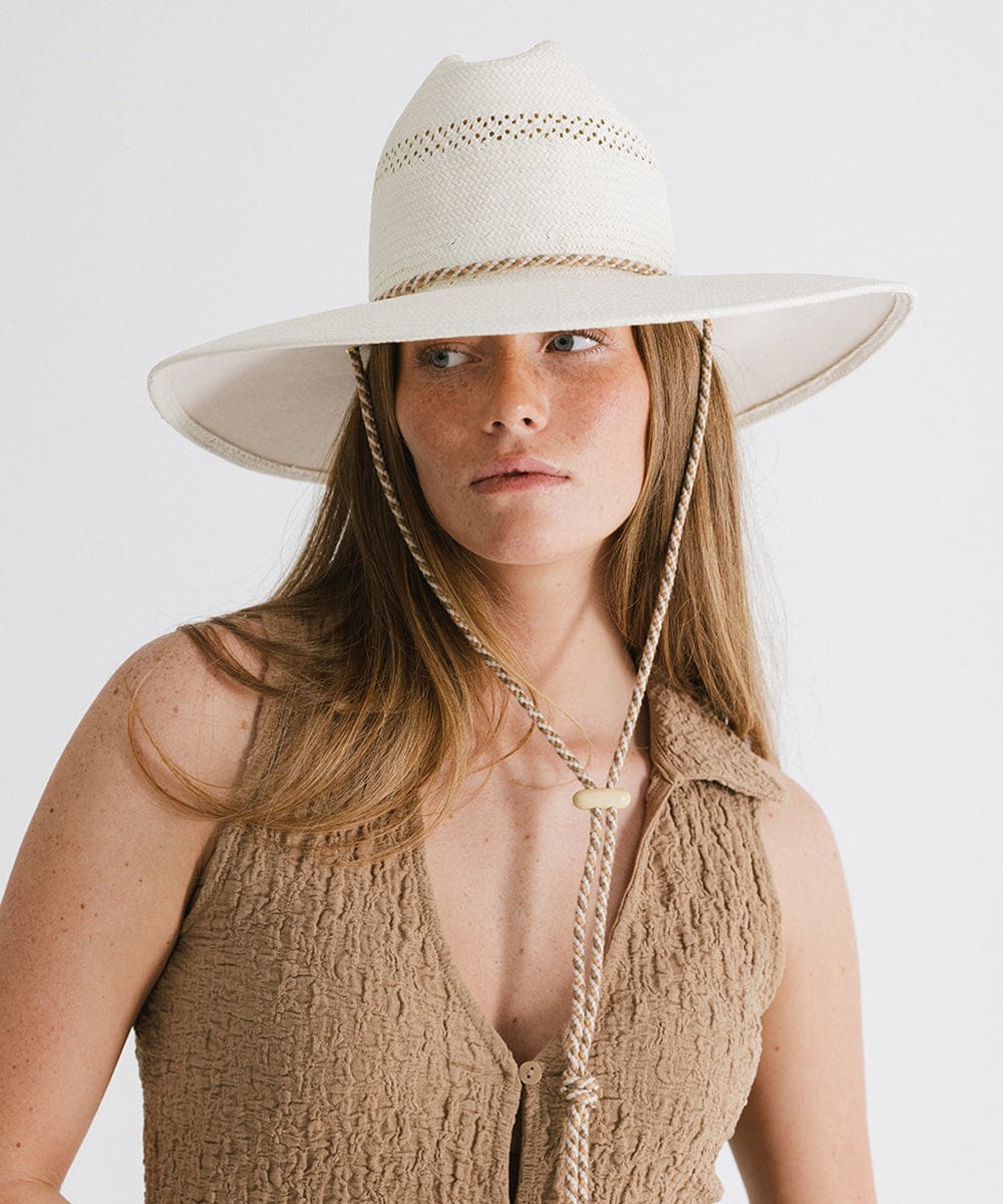 Woman wearing a cream straw hat with a rope hat band and a brown top against a plain background #color_cream