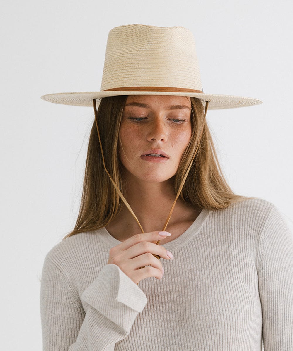 Woman wearing an ivory palm straw sun hat with a brown chinstrap and a white t-shirt against a plain background #color_ivory