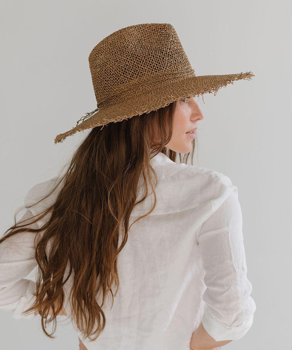 Woman wearing a brown straw fedora hat with a band and a white shirt, looking sideways against a plain background #color_brown