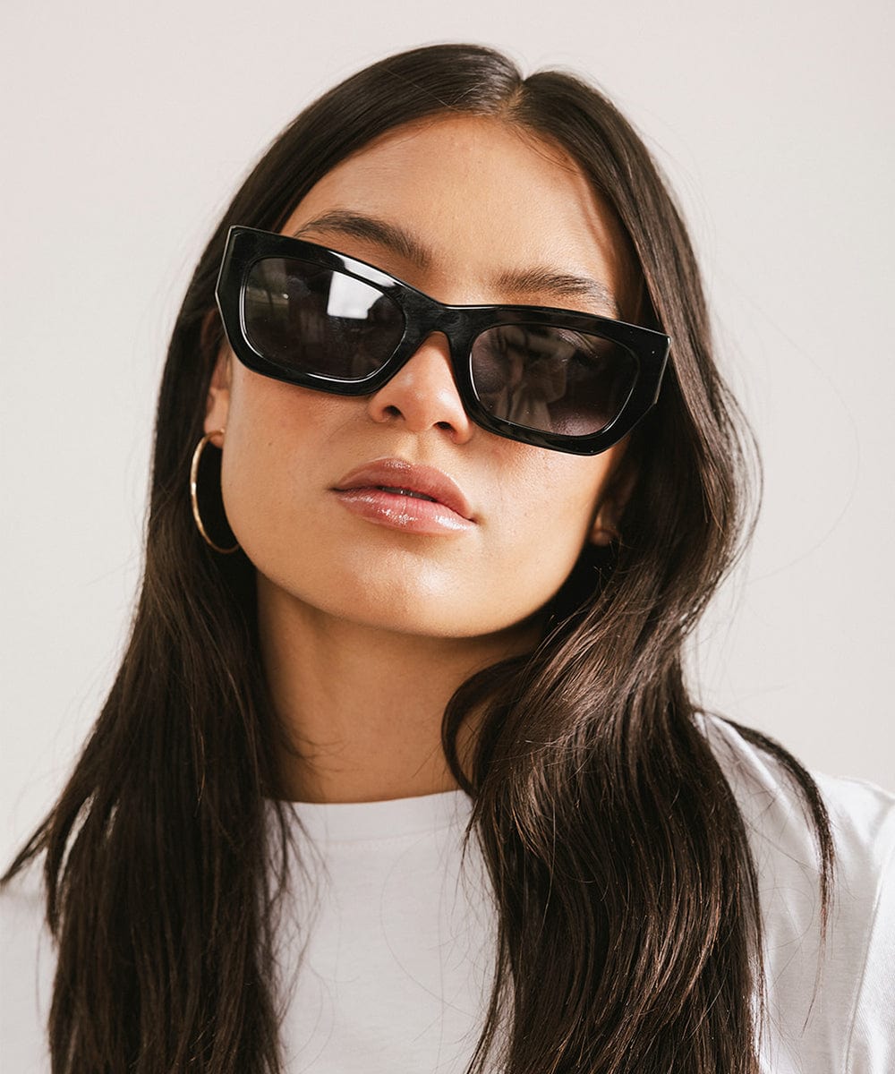 Woman wearing black sunglasses and a white t-shirt against a plain background #color_black