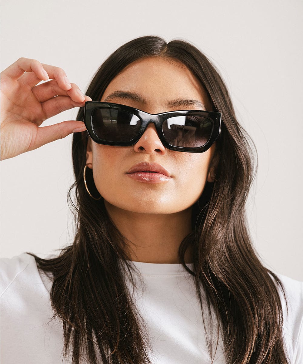 Woman wearing black sunglasses and a white t-shirt against a plain background #color_black