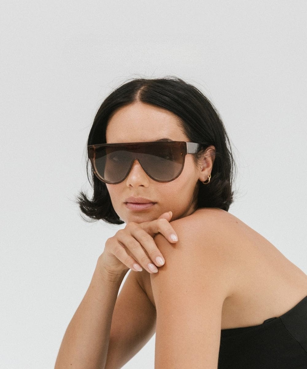 Woman wearing amber colored sunglasses and a black top against a plain background #color_amber