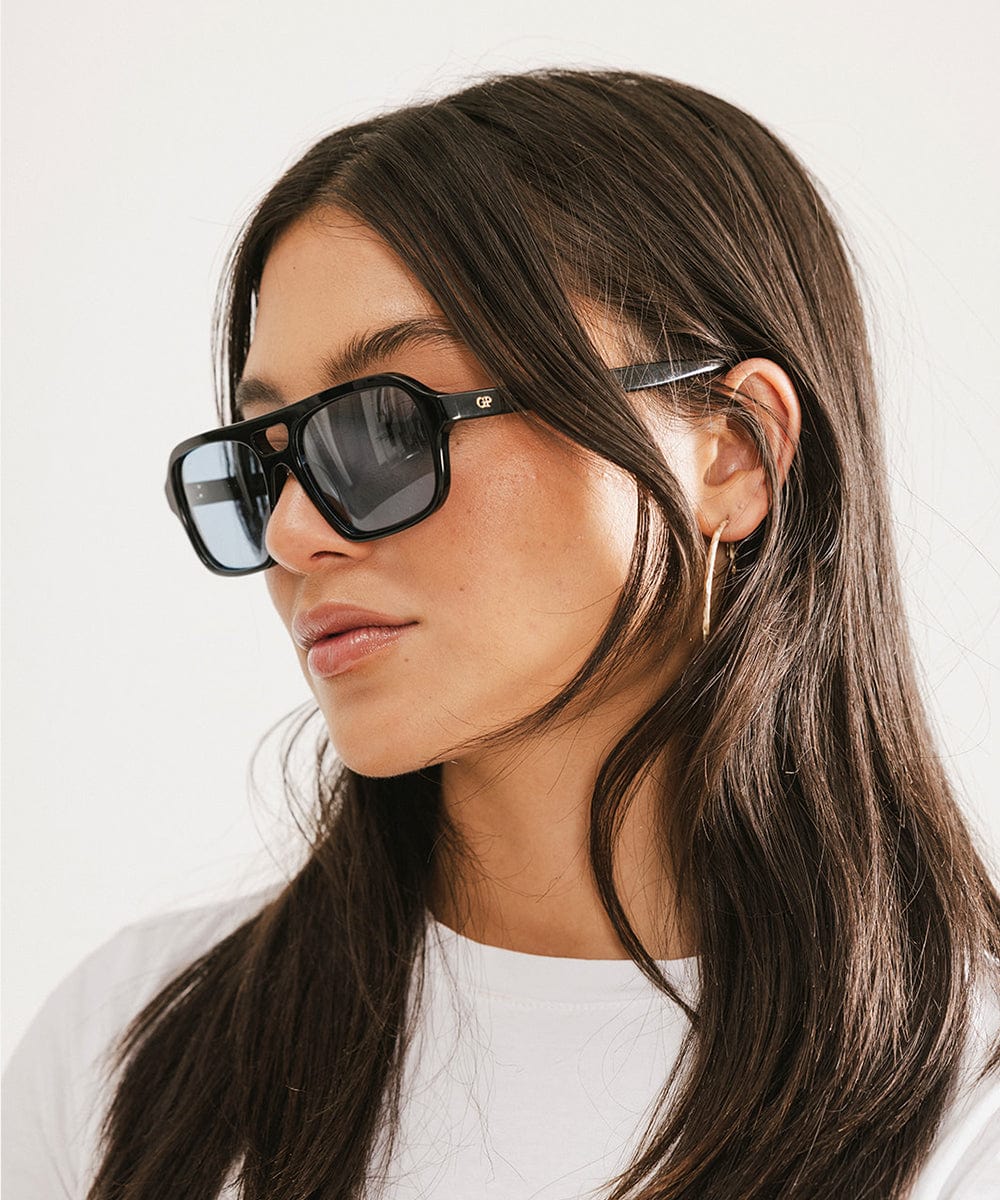 Woman wearing black sunglasses and a white t-shirt, facing sideways against a plain background #color_black