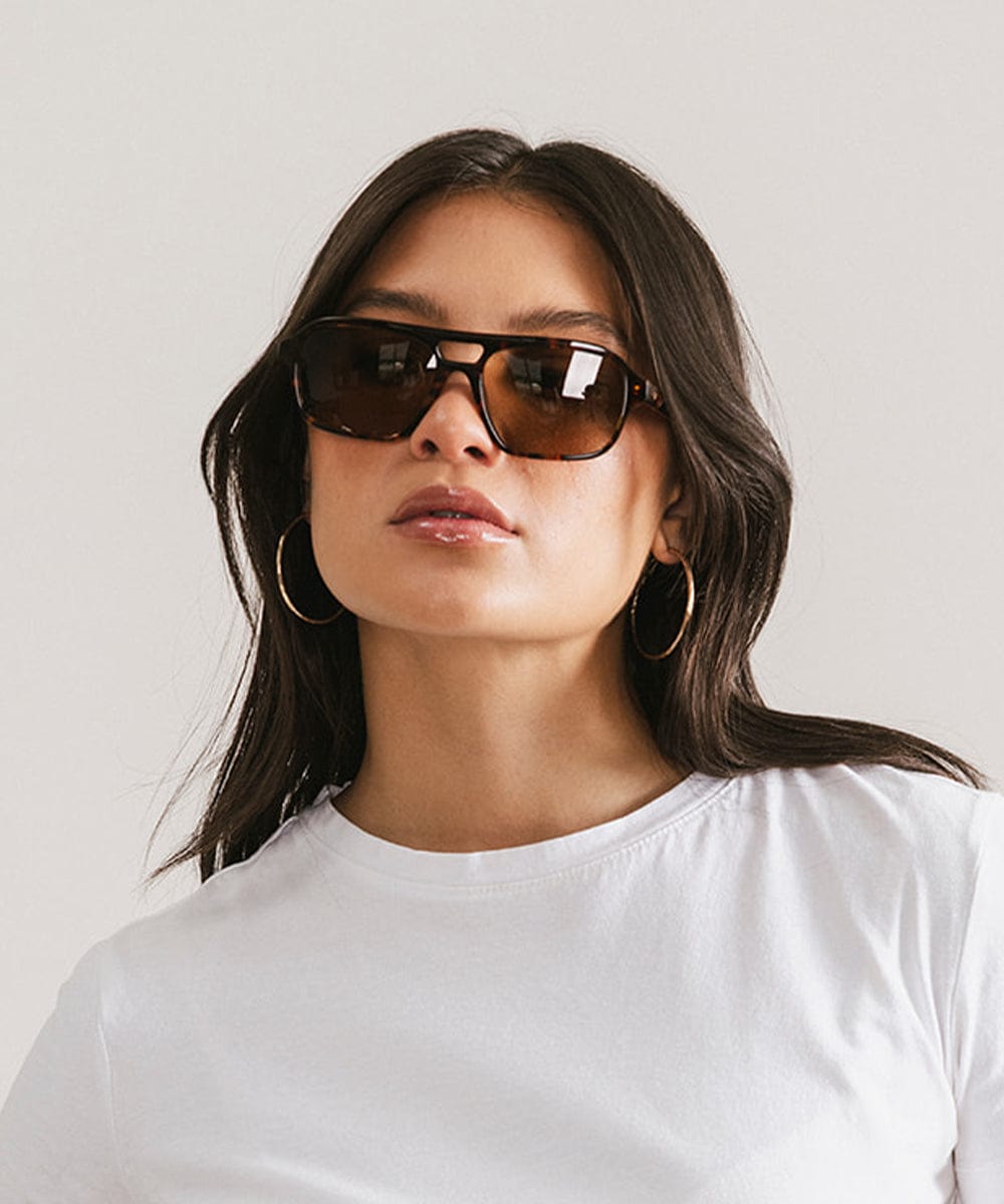 Woman wearing sunglasses and a white shirt against a plain background #color_tortoise