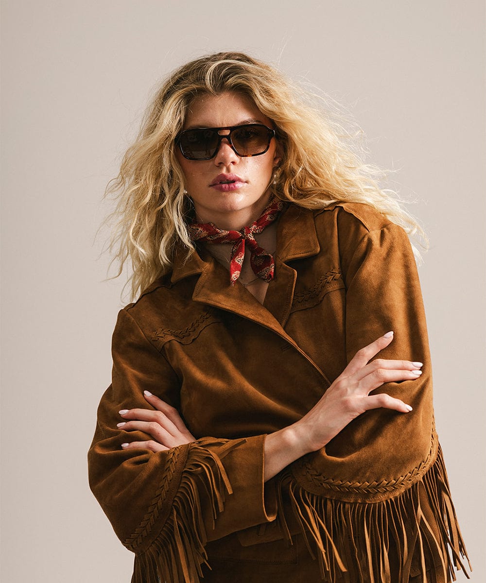 Woman wearing a brown suede jacket with fringe, sunglasses, and a red scarf against a plain background #color_tortoise