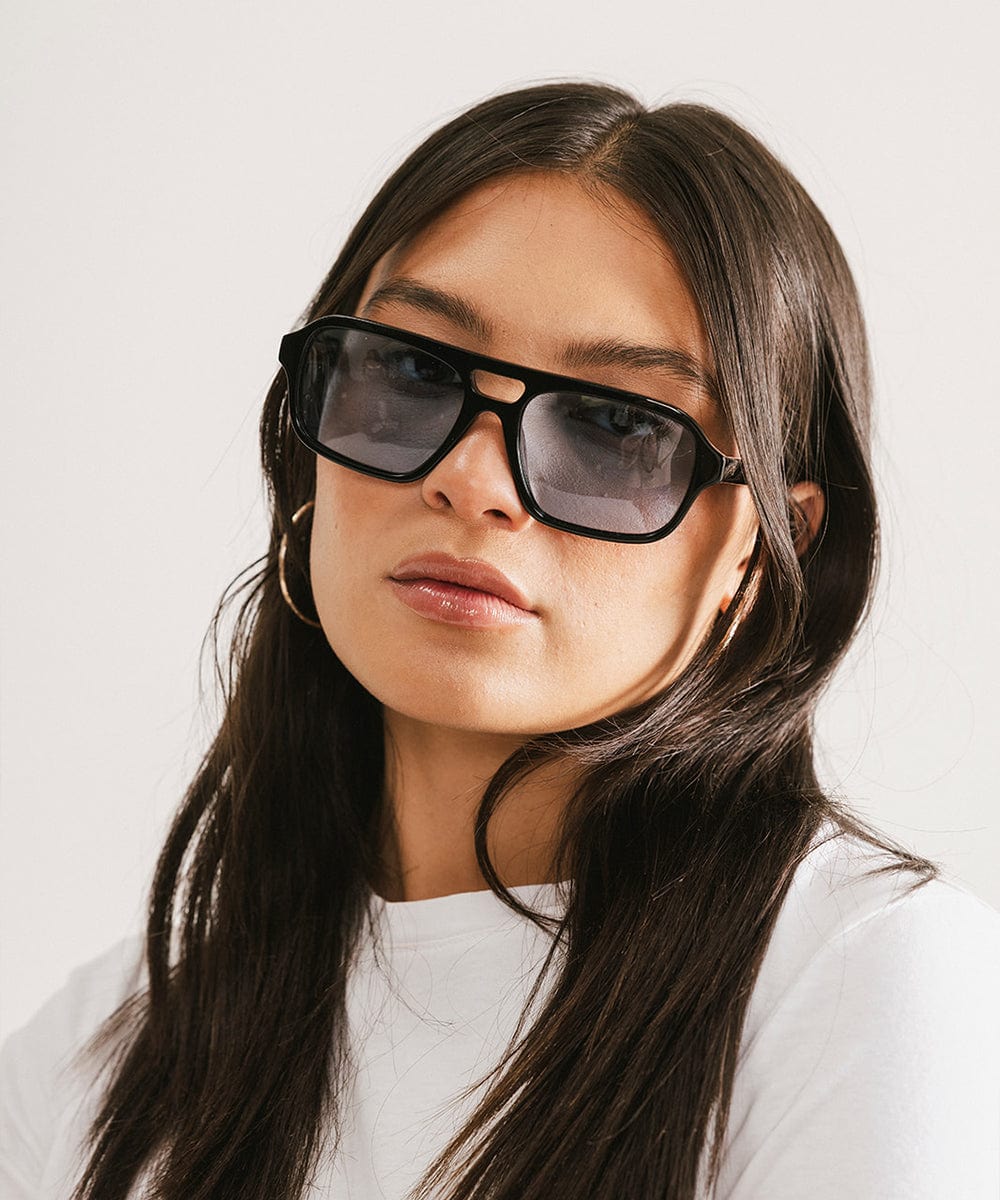 Woman wearing black sunglasses and a white t-shirt against a plain background #color_black