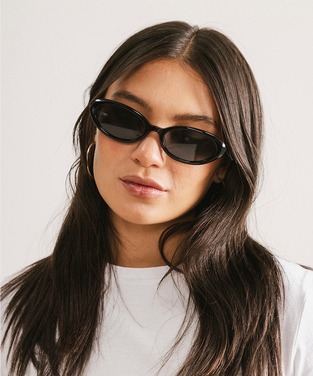 Woman wearing black sunglasses and a white t-shirt against a plain background #color_black