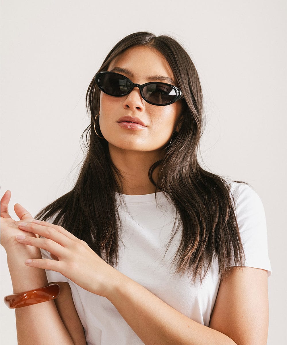 Woman wearing black sunglasses and a white t-shirt, posing against a plain background #color_black