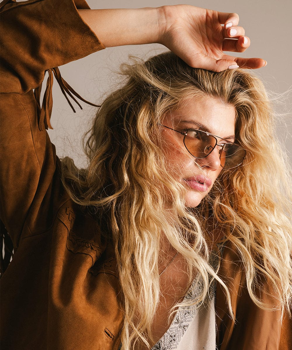 Woman wearing brown sunglasses and a brown coat, facing sideways against a neutral background #color_brown