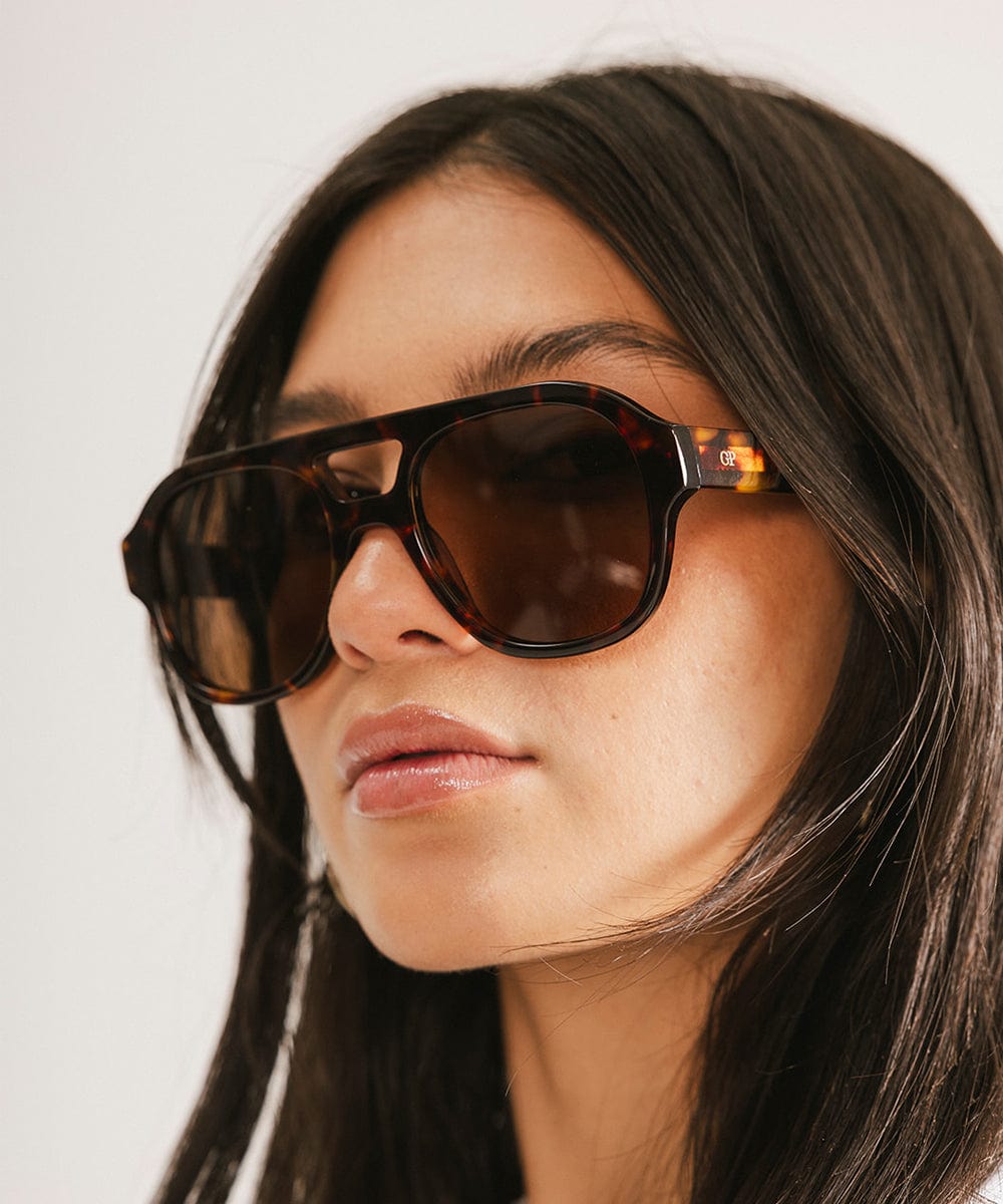 Woman wearing tortoise colored aviator sunglasses against a plain background #color_tortoise