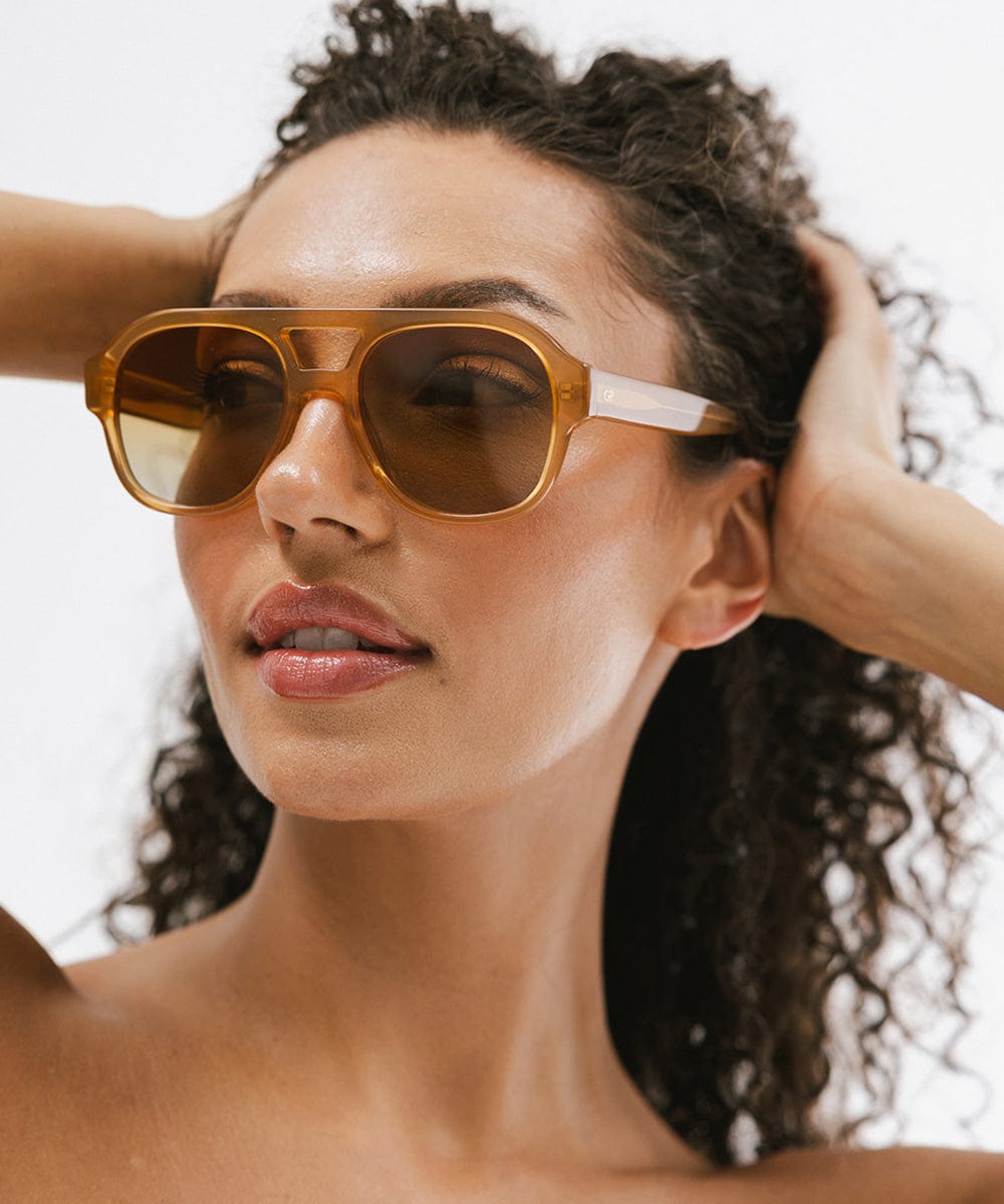 Woman wearing honey colored aviator sunglasses against a plain background #color_honey