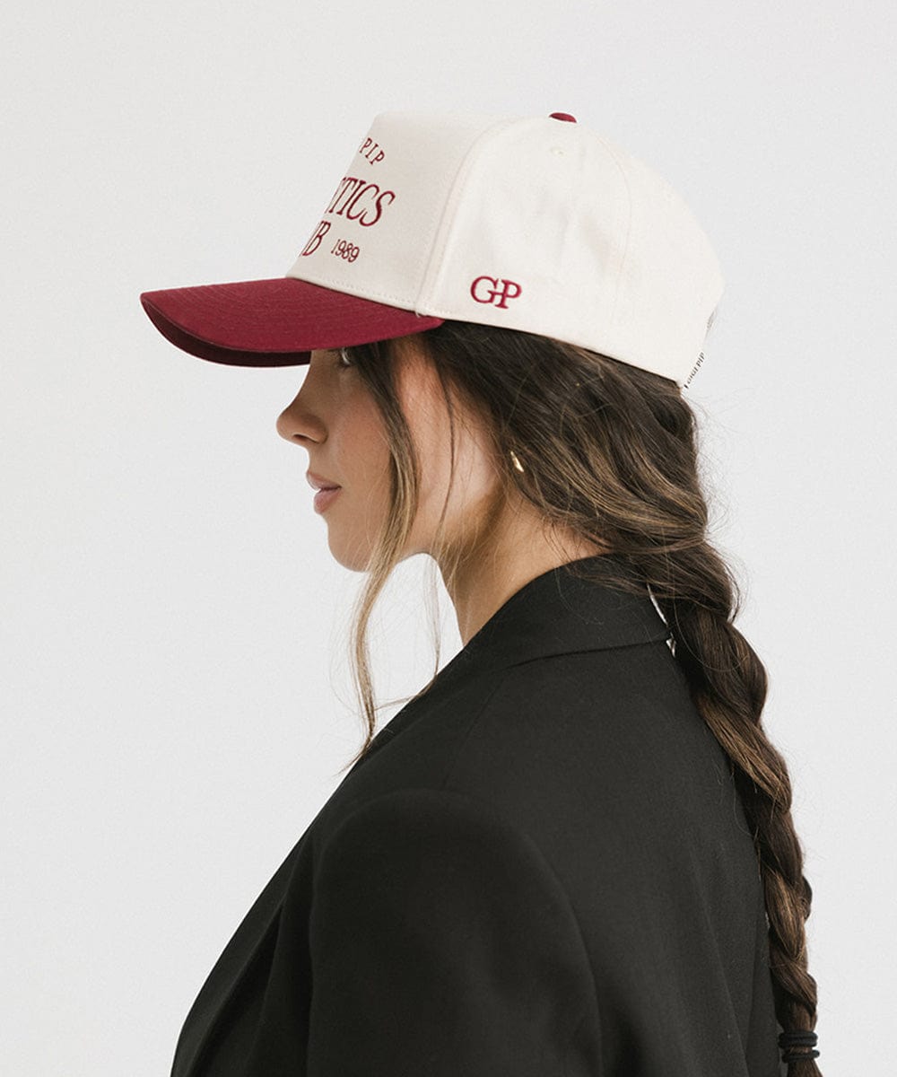 Woman wearing a Burgundy Trucker hat and a black coat, posing sideways against a plain background #color_burgundy
