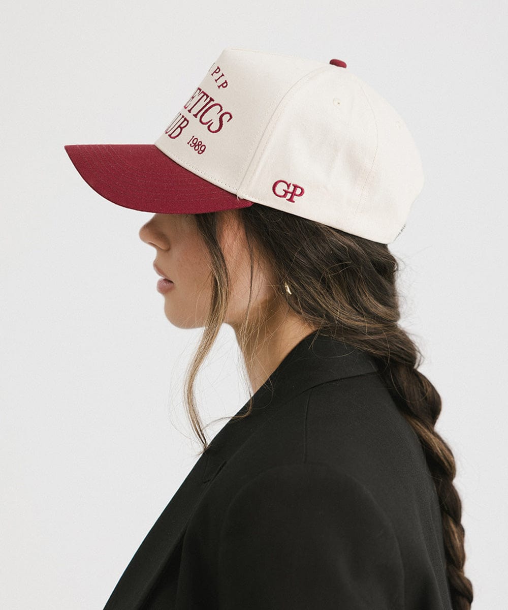 Woman wearing a Burgundy Trucker hat and a black coat, facing sideways against a plain background #color_burgundy