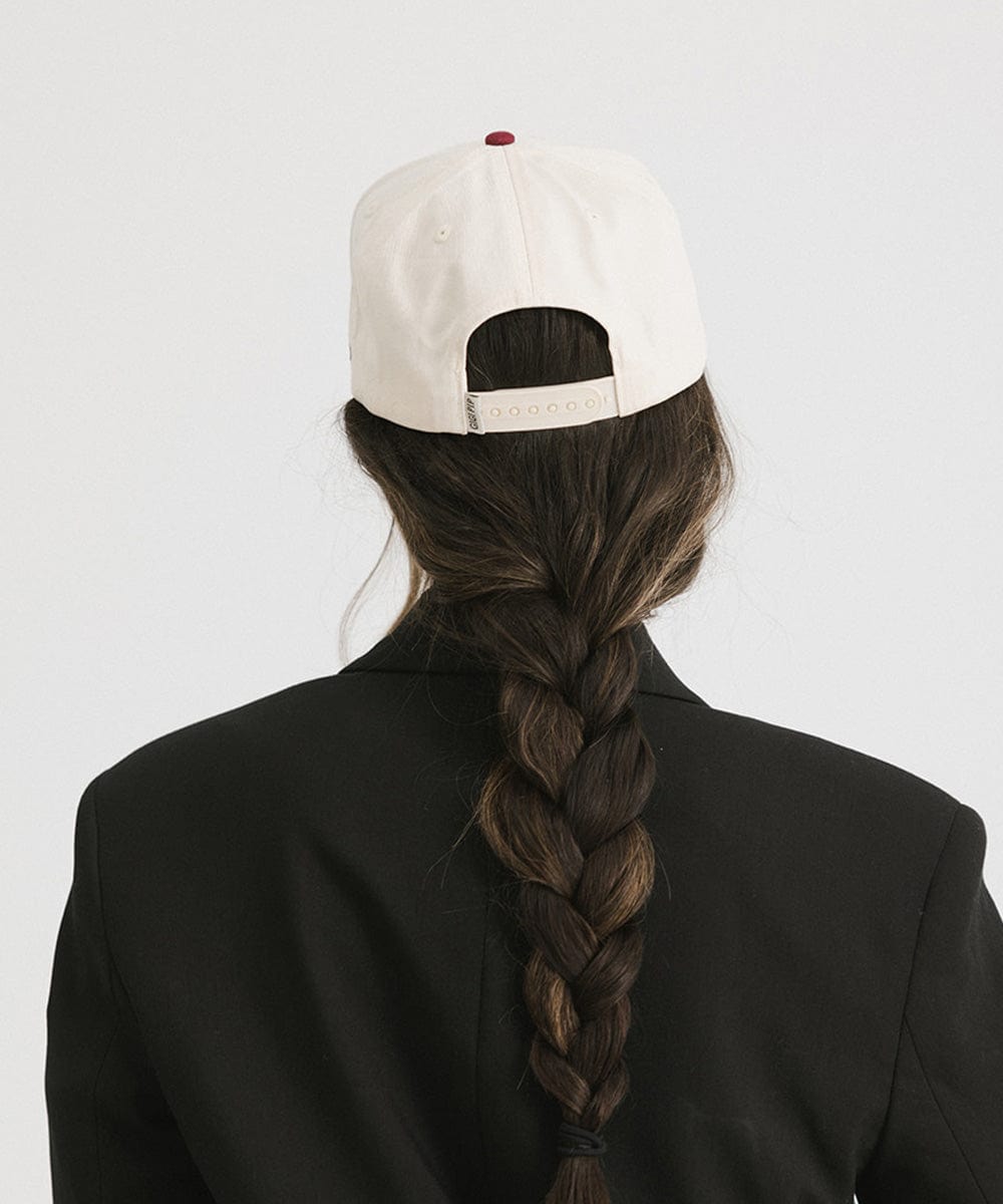 Woman wearing a burgundy Trucker hat and a black coat against a plain background #color_burgundy