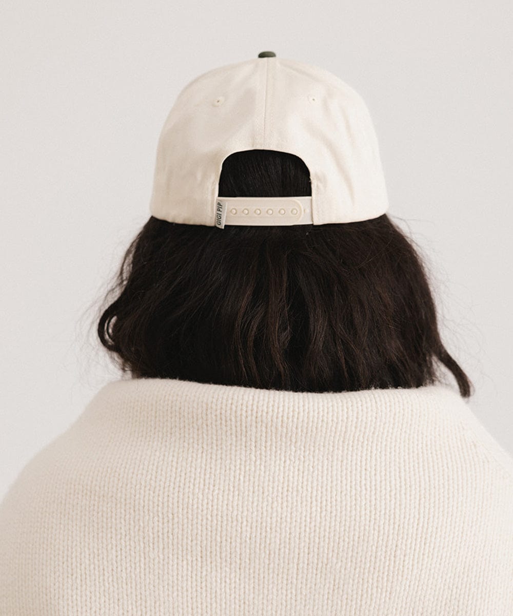 Person wearing a cream and dark green Trucker hat against a plain background #color_cream - dark green