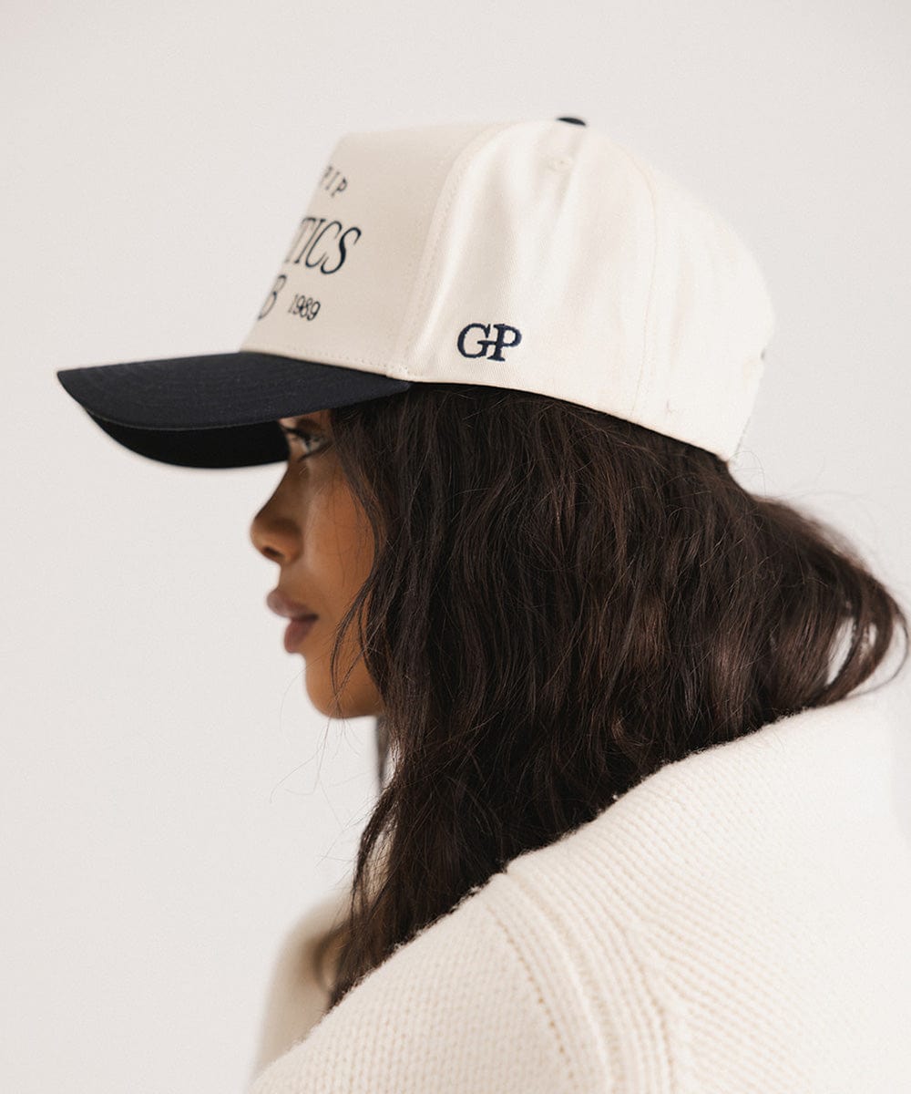 Woman wearing a Navy Trucker hat and a white sweater, facing sideways against a plain background #color_navy