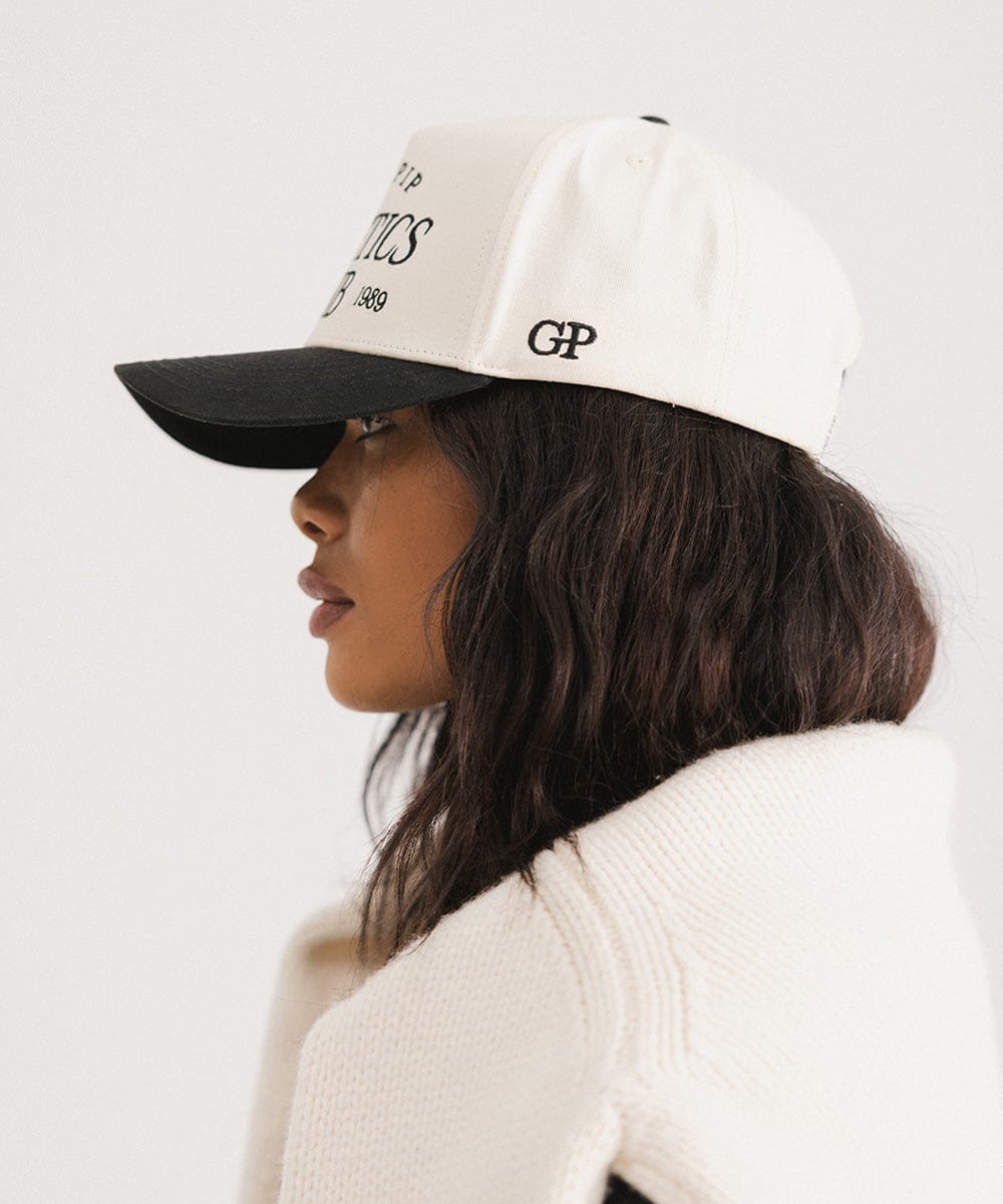 Woman wearing a cream and black Trucker hat and a white sweater, facing sideways against a plain background #color_cream - black