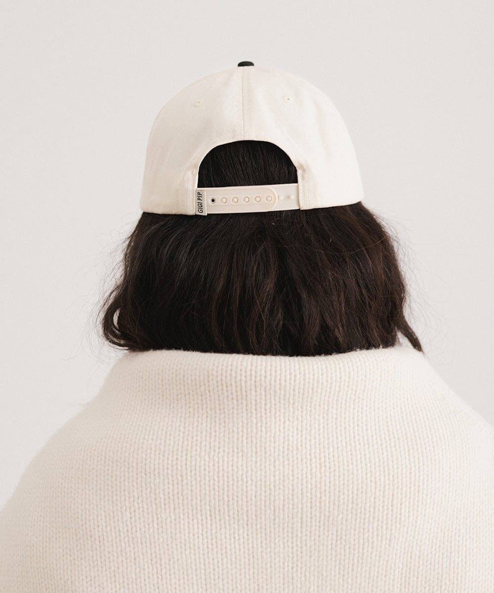 Person wearing a cream and black Trucker hat and a white sweater against a plain background #color_cream - black