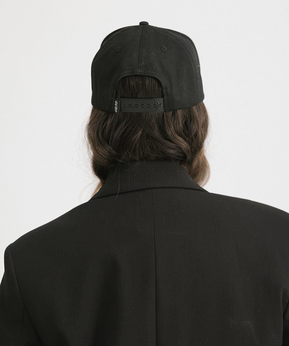 Person wearing a Black Trucker hat and a black blazer against a plain background #color_black