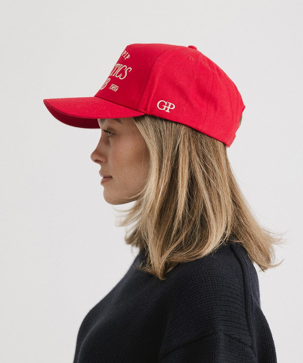 Woman wearing a Red Trucker hat and a dark blue sweater, facing sideways against a plain background #color_red