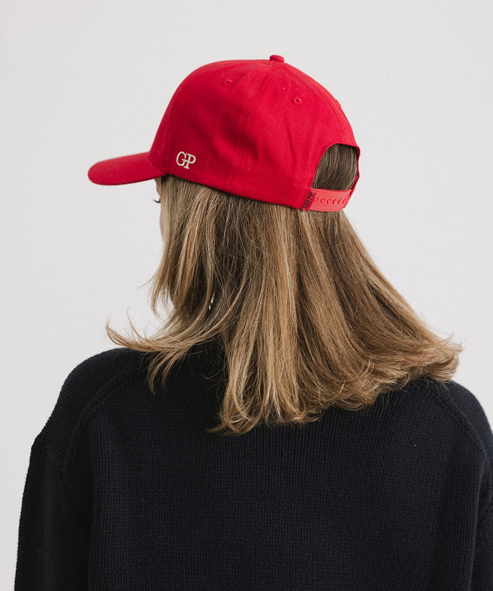Woman wearing a Red Trucker hat and a dark blue sweater against a plain background #color_red