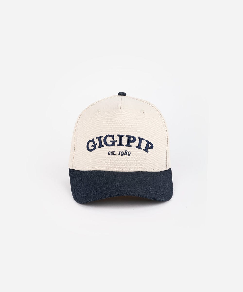 A cream and navy trucker hat with 'GIGI PIP' embroidered in navy on the front against a plain background #color_cream - navy