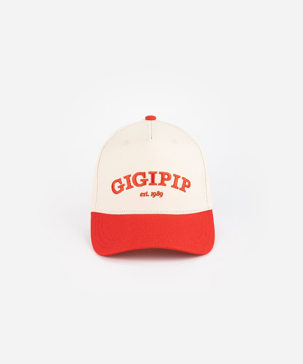 A cream and red trucker hat with 'GIGI PIP' embroidered in red on the front against a plain background #color_cream - red