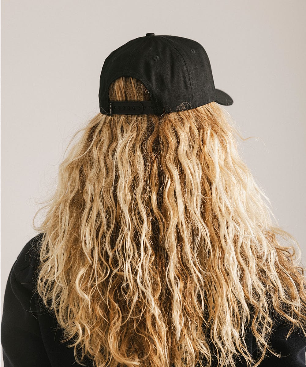 Woman with long hair wearing a black vintage trucker cap against a plain background #color_black