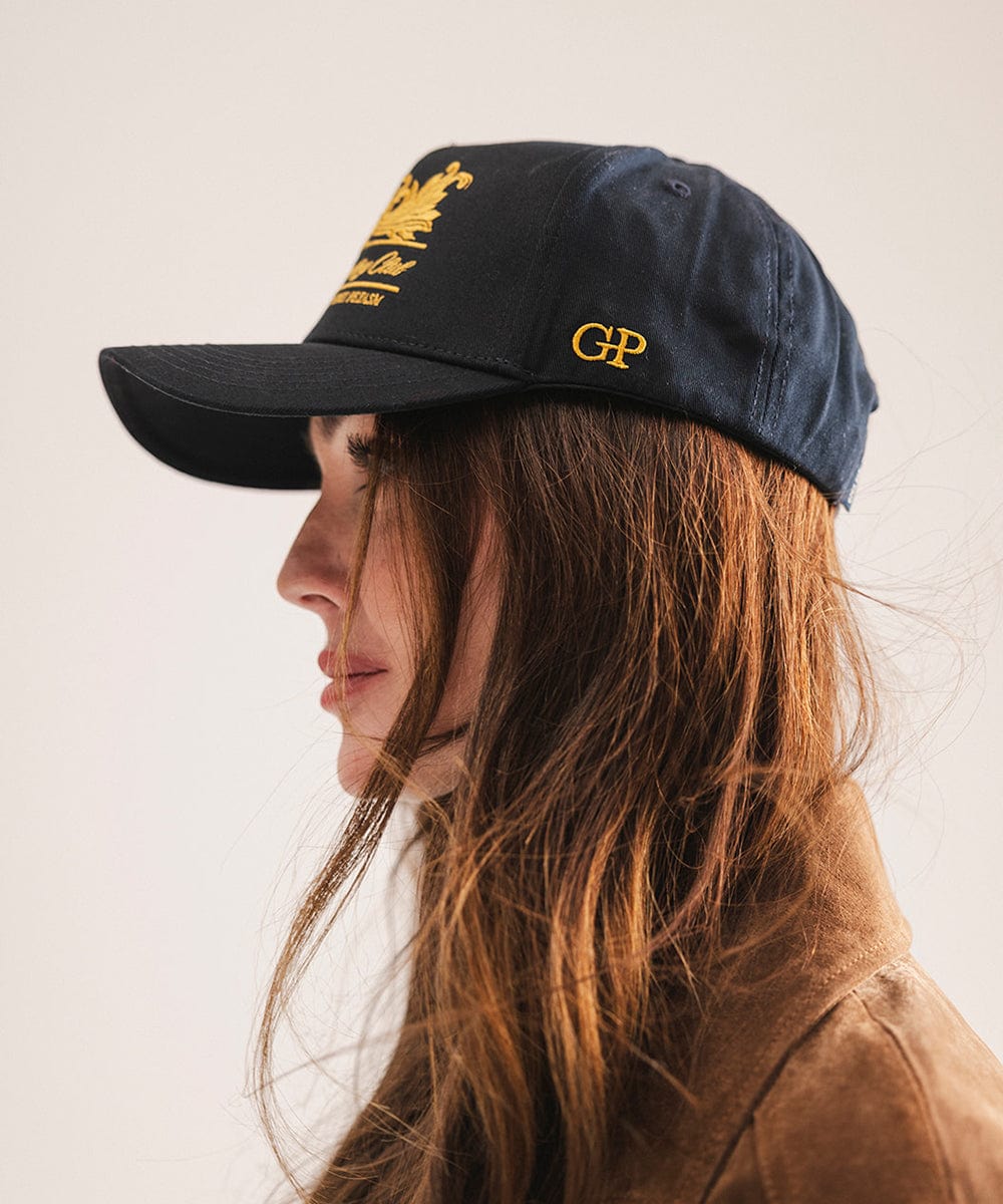 Person wearing a navy blue cap with gold logo and text on a plain background #color_navy