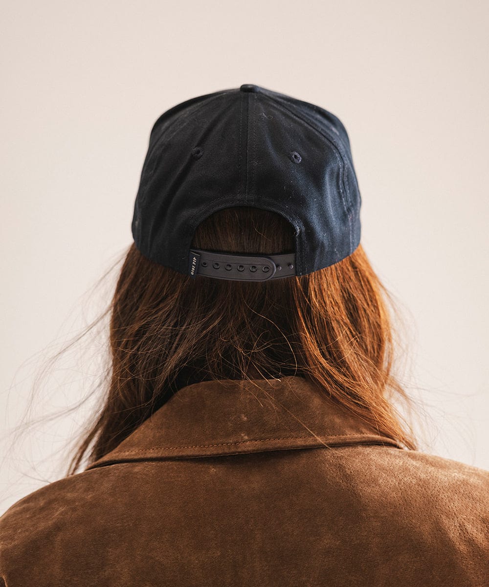Person wearing a navy blue cap and brown jacket from behind on a light background #color_navy