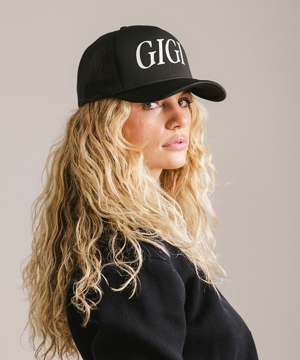 Woman wearing a black cap with 'GIGI' text and a black shirt, posing sideways against a plain background #color_black