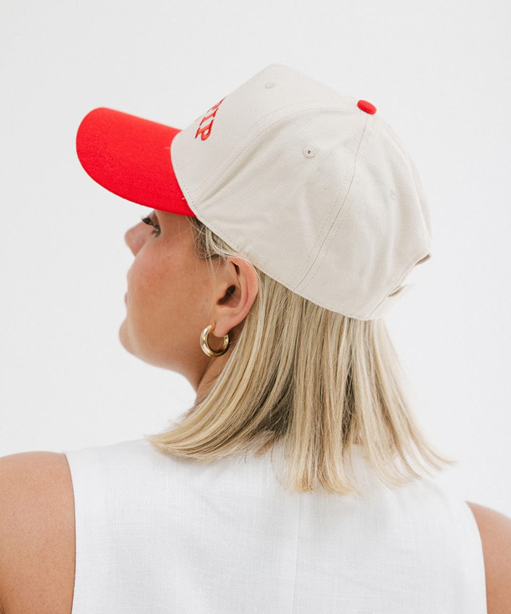 Woman wearing a cream and red trucker hat with 'GIGI PIP' embroidered in red on the front and a white top, posing against a plain background #color_cream - red