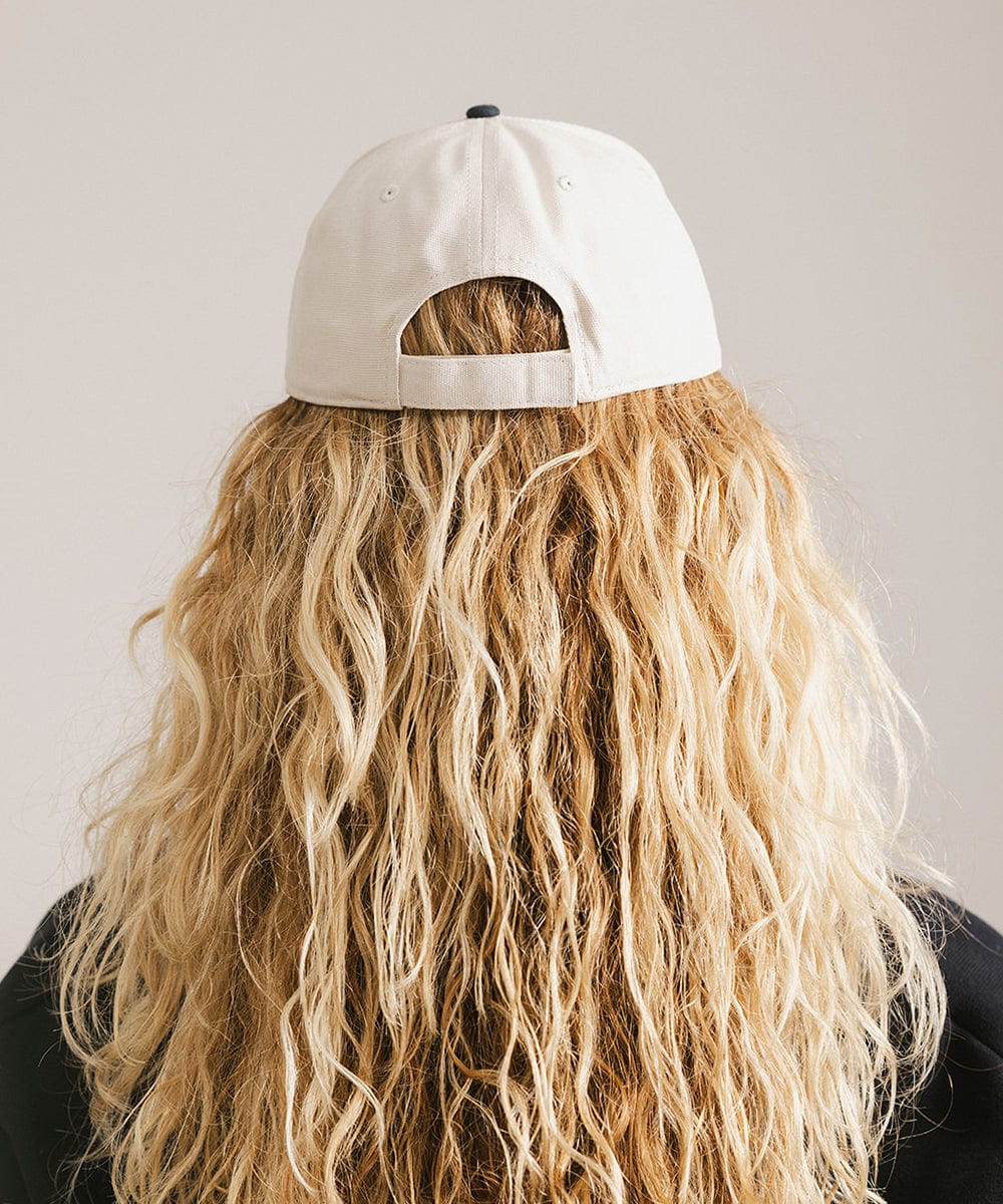 Woman with long hair wearing a cream and navy trucker hat against a plain background #color_cream - navy