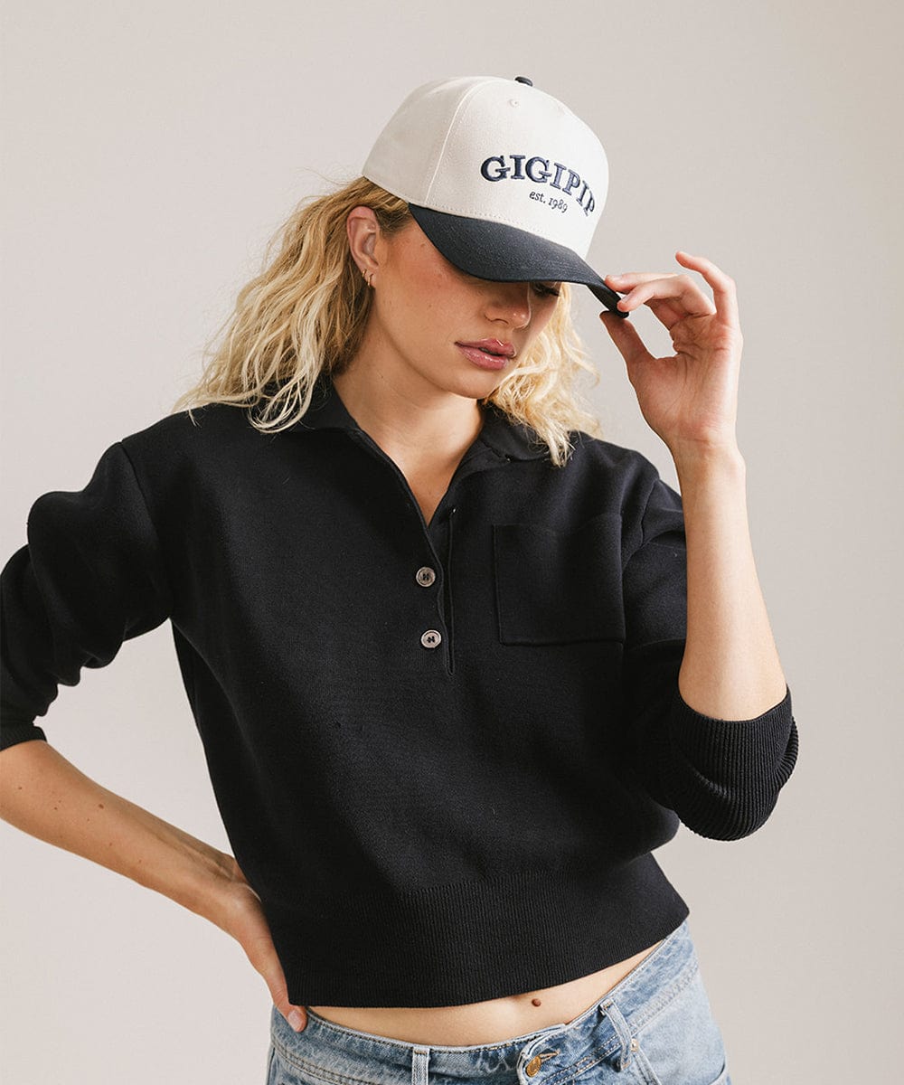 Woman wearing a cream and navy trucker hat with 'GIGI PIP' embroidered in navy on the front and a black shirt, posing against a plain background #color_cream - navy
