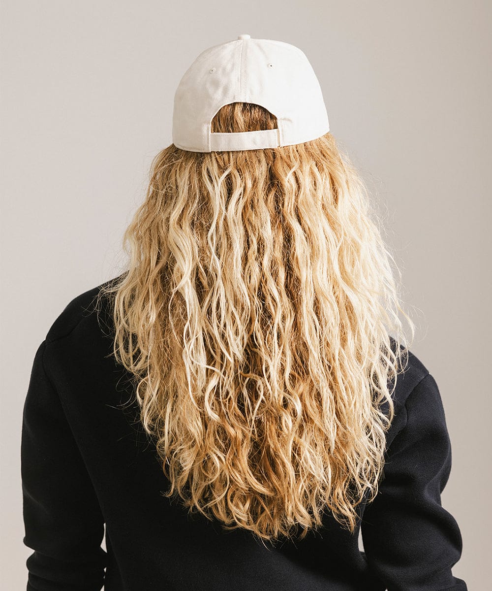 Woman with long blonde hair wearing a cream cap and a black shirt against a plain background #color_cream