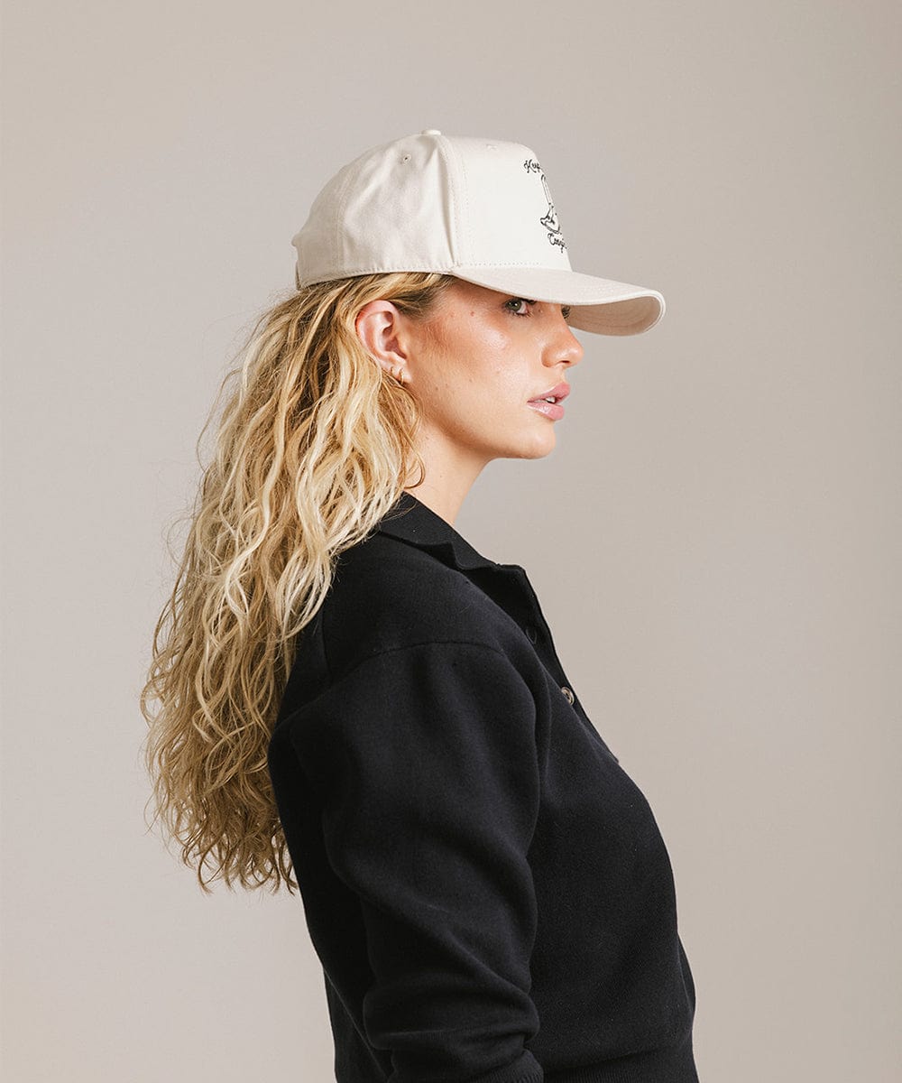 Woman wearing a cream cap and a black shirt, facing sideways against a plain background #color_cream