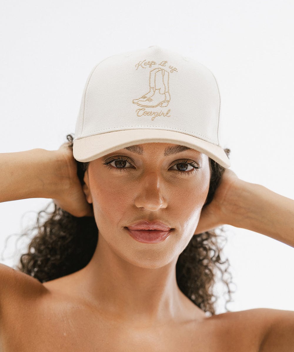 Woman wearing a cream and tan cap with tan text and boot design against a plain background #color_cream - tan