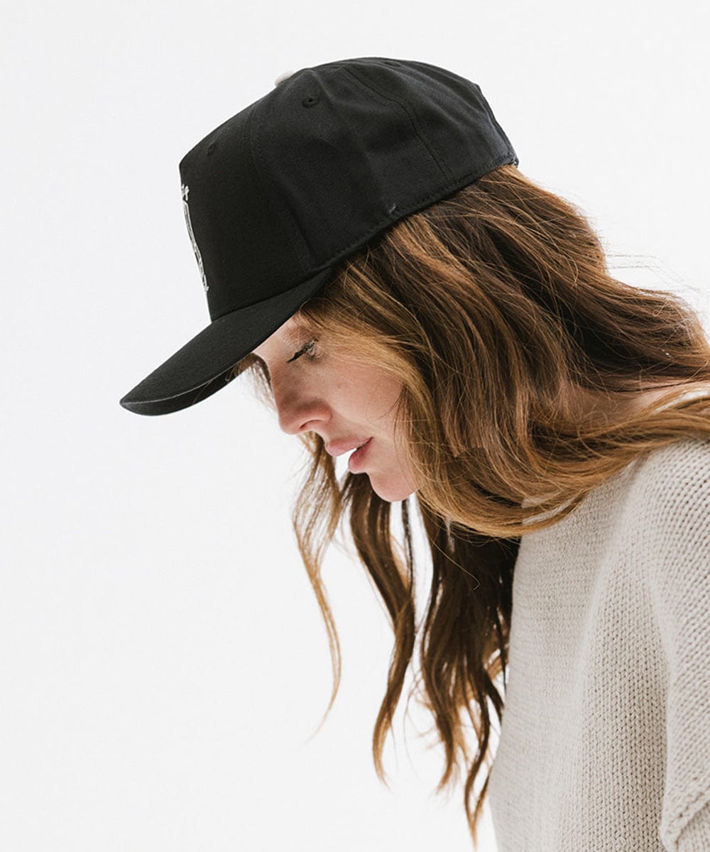 Woman wearing a black cap and an off white t-shirt, posing against a plain background #color_black