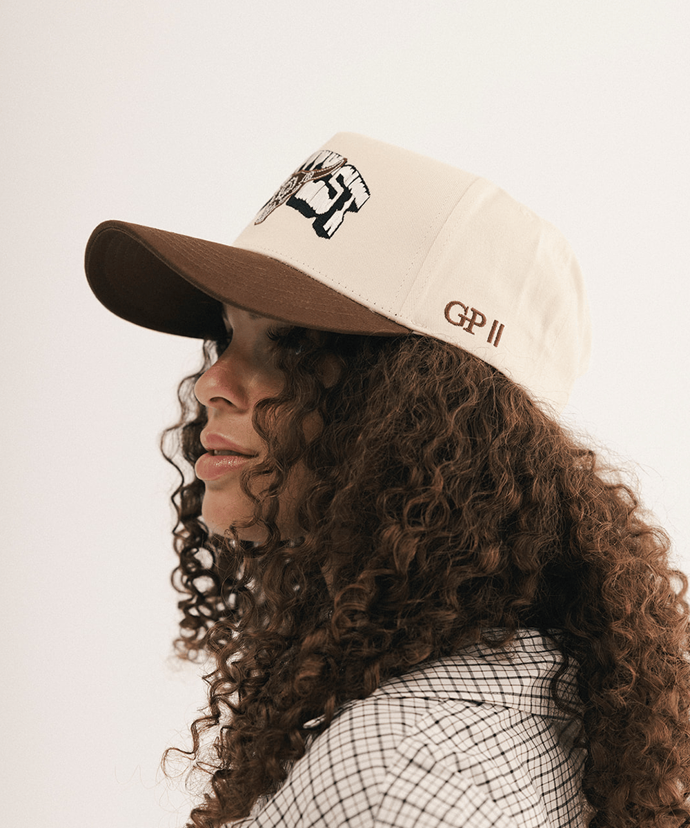 Woman's side view wearing a beige and brown cap with bull logo on a white background #color_cream - brown