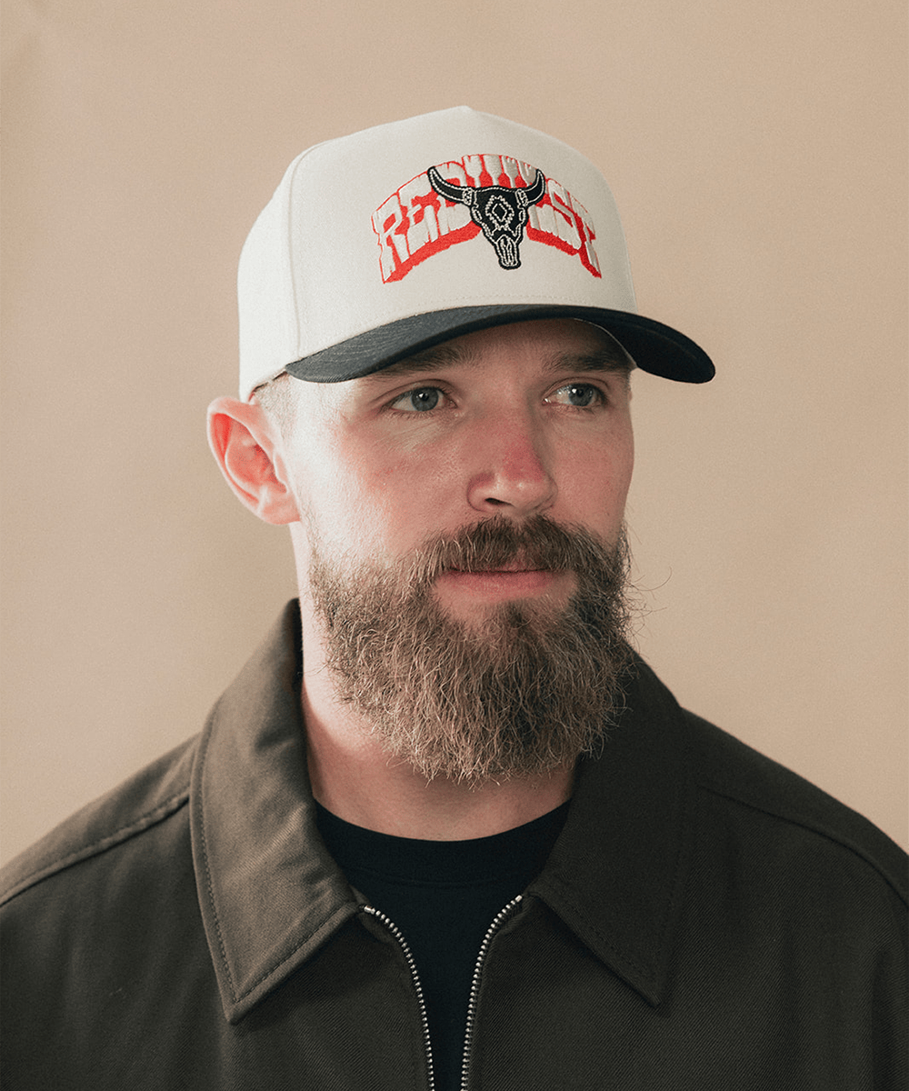 Man wearing a beige and black cap with bull logo on a plain background #color_cream - black