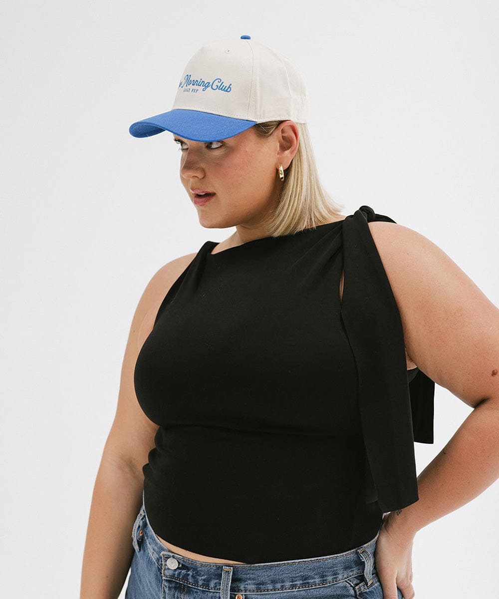 Woman wearing a cream and blue cap with 'Slow Morning Club' text and a black top, facing sideways against a plain background #color_cream - blue