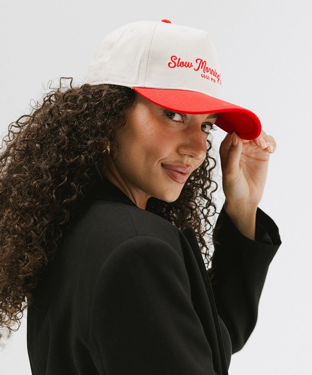 Woman wearing a cream and red cap with 'Slow Morning Club' text and a black coat, facing sideways against a plain background #color_cream - red