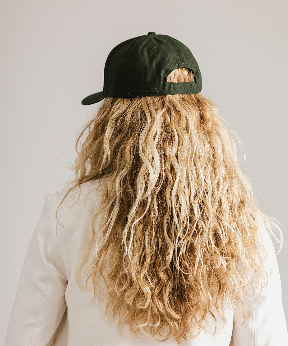Woman with long hair wearing a dark green cap and a white coat against a plain background #color_dark green