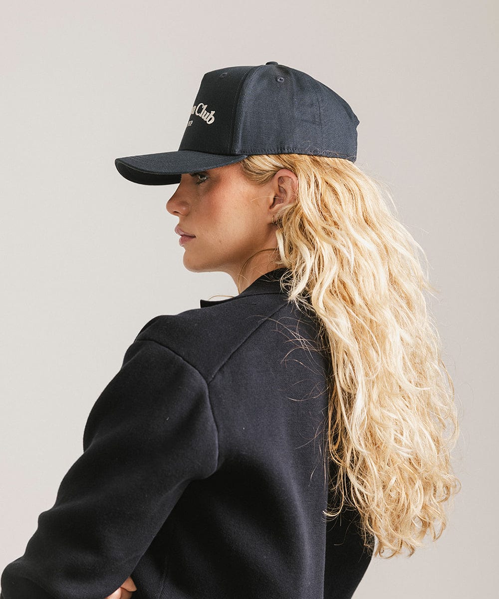 Woman wearing a navy cap with 'Vacation Club' text and a black shirt, facing sideways against a plain background #color_navy